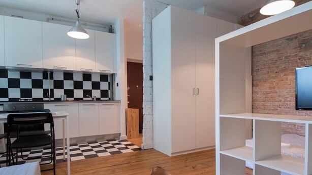 A modern kitchen with white cabinets, a black and white checkered floor, and a wooden dining table with chairs. - Bizzi LuxProchnika Studio (Warsaw)