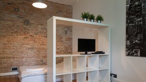 A modern room with a brick wall, a white shelving unit with a flat-screen TV, a bed with white bedding, and a cowhide rug. - Bizzi LuxProchnika Studio (Warsaw)