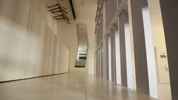 Un pasillo largo y estrecho con perchas de madera a la izquierda y una escalera a la derecha.