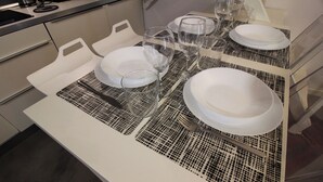 Una mesa de comedor con platos blancos, vasos transparentes y cubiertos sobre un mantel estampado.