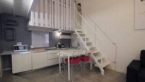 Cocina compacta con microondas, fregadero y un pequeño comedor con mesa y sillas.