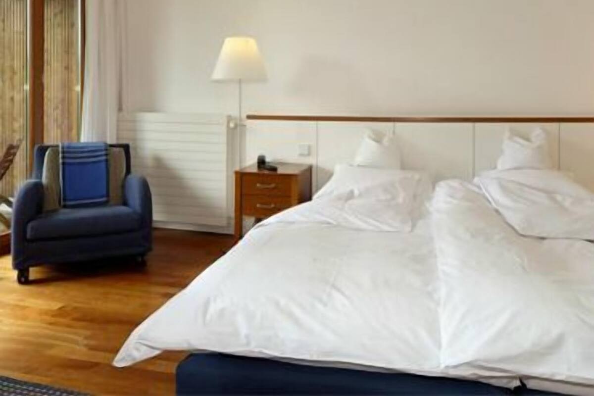 Une chambre d’hôtel avec un lit, une chaise, une table de chevet et une lampe.