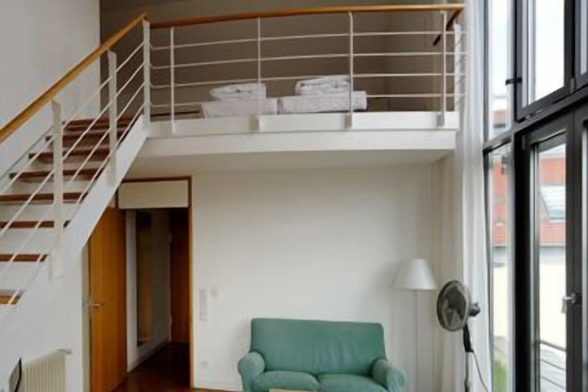Un vaste espace de vie doté d’un haut plafond, d’un escalier, d’un canapé vert, d’une petite table et d’un lampadaire.