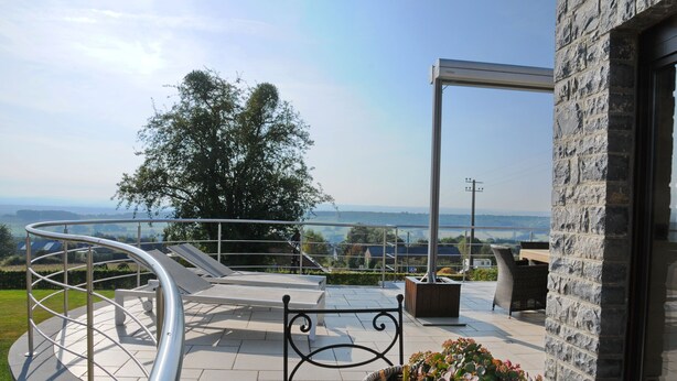 Une terrasse sur le toit, dotée d’une rambarde métallique incurvée, d’un banc et d’un pot de fleurs.