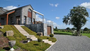 Une maison moderne avec une façade en pierre, une porte en bois et un escalier menant à un porche abrité.