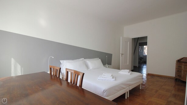 A bedroom with a wooden bed, white linens, a wooden table, and a chair. - Italianway   - Piacenza (Milan)