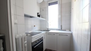 A compact kitchen with white cabinets, a stove, an oven, a sink, and a window with blinds. - Italianway   - Piacenza (Milan)