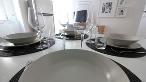 A dining table set with plates, bowls, and wine glasses, with a refrigerator and framed pictures in the background. - Italianway   - Piacenza (Milan)