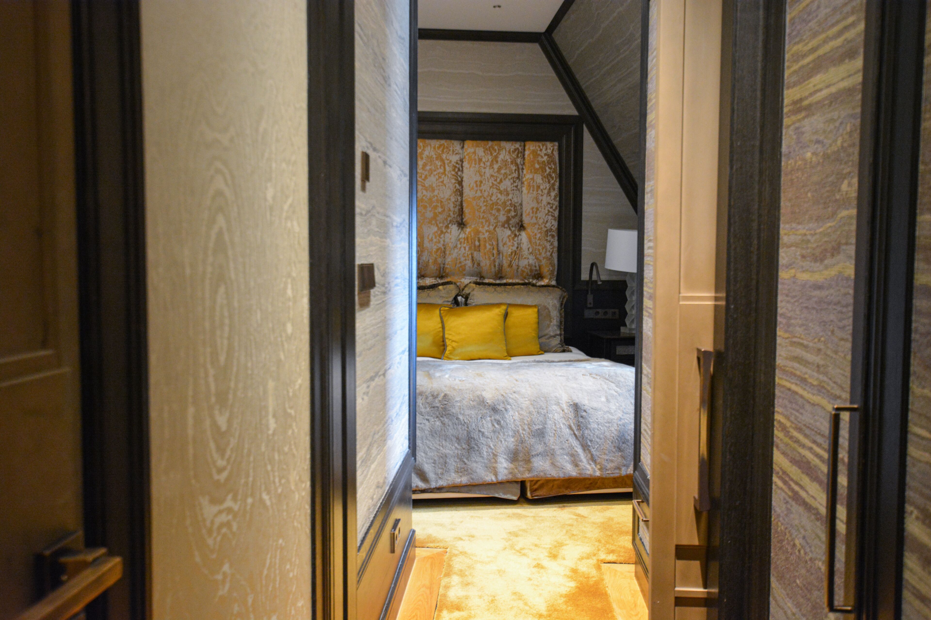 Un pasillo estrecho que conduce a un dormitorio con una cama, una mesita de noche y una lámpara.