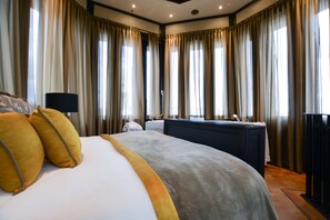 Habitación de hotel con una cama grande, un escritorio con lámpara y vistas a la ciudad a través de las ventanas.