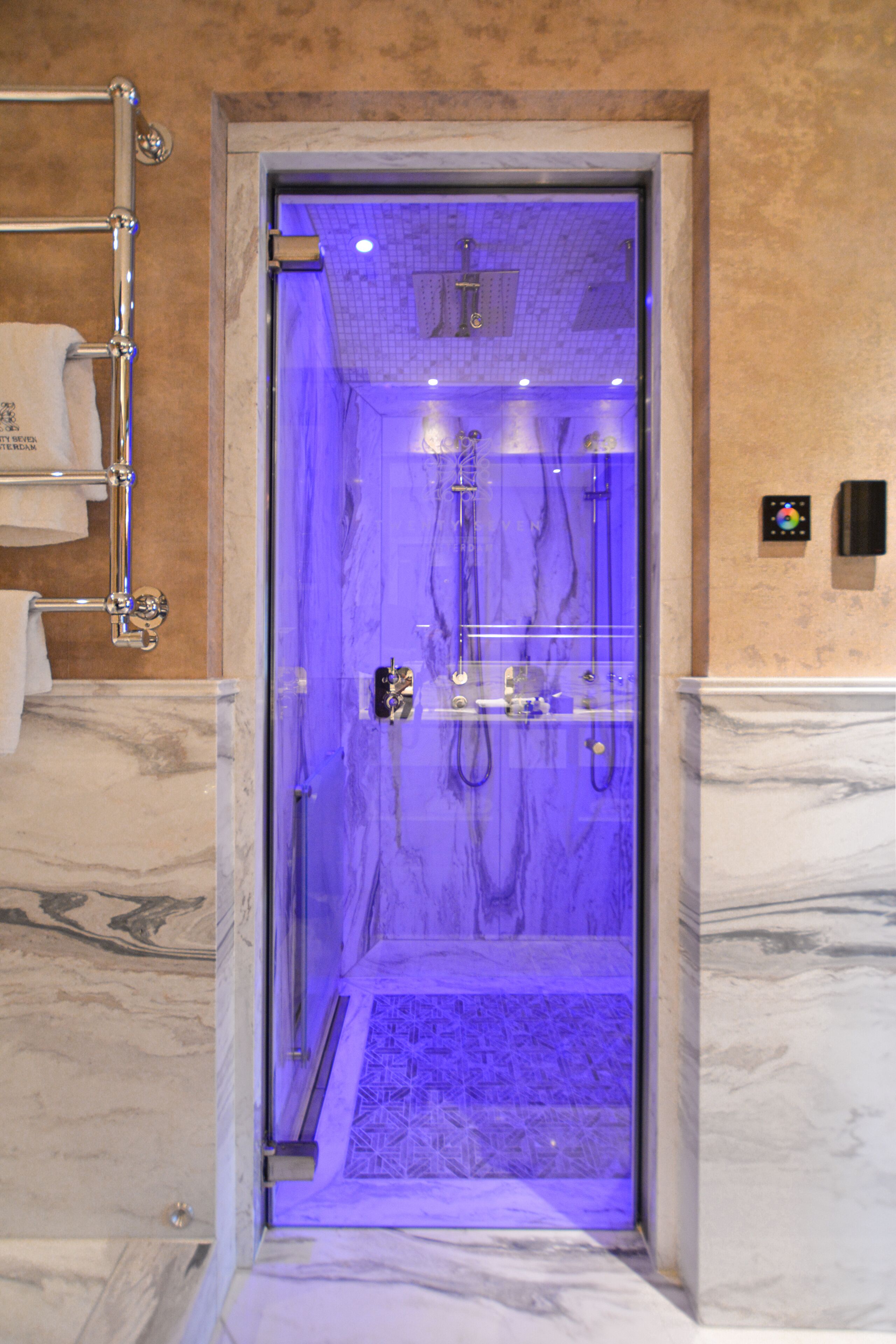 A glass-enclosed shower with a marble floor and a towel rack to the left.