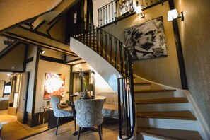 A staircase with a black railing, a painting on the wall, and a seating area with a table and chairs.