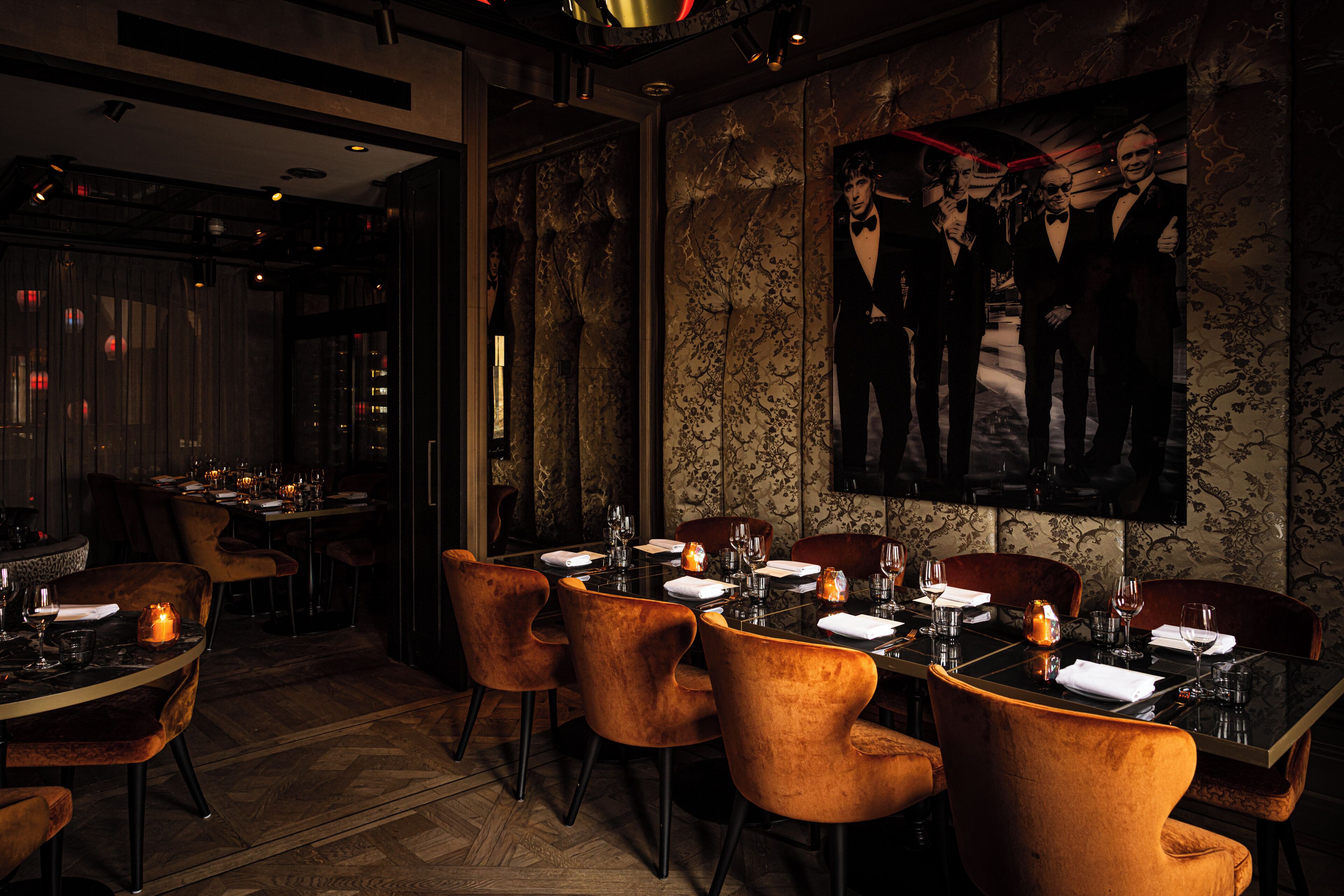 Un restaurant à la lumière tamisée, avec des fauteuils en velours, une table élégante et un grand portrait encadré accroché au mur.