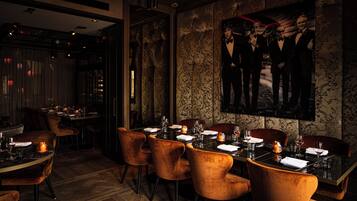 Un restaurant à la lumière tamisée, avec des fauteuils en velours, une table élégante et un grand portrait encadré accroché au mur.