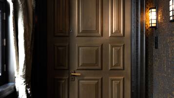 A closed door with a number sign above it, a patterned carpet, and a wall with a textured finish.