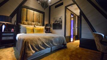 A bedroom with a large bed, a chandelier, and a door leading to another room.