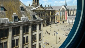 Vista a través de un ventanal circular que muestra un paisaje urbano con edificios históricos, una cúpula central y un cielo azul despejado.