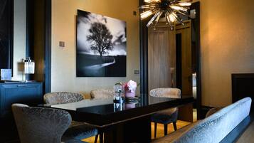 A modern dining area with a long table, patterned chairs, and a wall-mounted artwork of a tree.