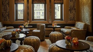 Una habitación lujosa con paneles de madera ornamentados, ventanas amplias con vistas a edificios y zonas de estar confortables.