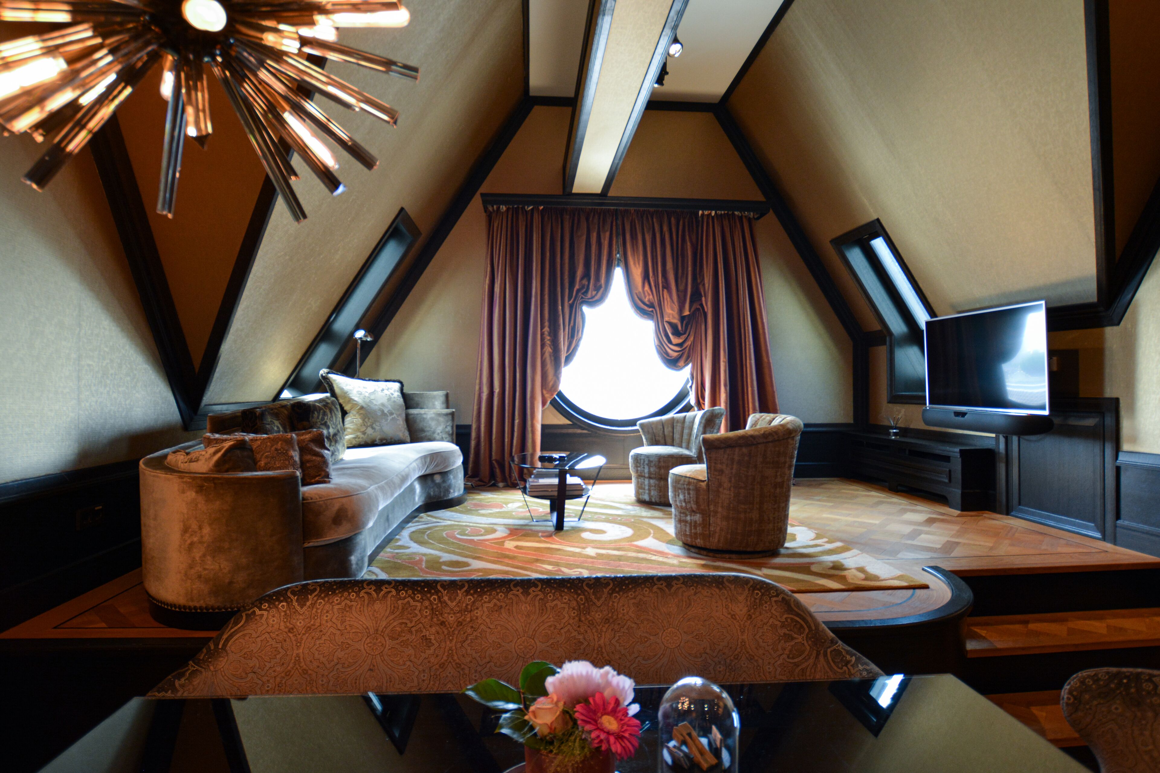 A cozy, triangular room with a sofa, chairs, a coffee table, and a television.