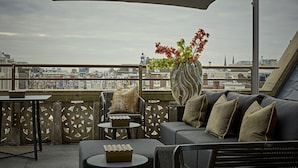 Una terraza en la azotea con un sofá, sillas, una mesa y un jarrón de flores.