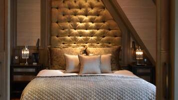 A bedroom with a tufted headboard, a bed with a quilted cover, a nightstand with a lamp, and a wooden floor.