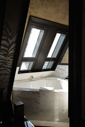 A bathroom with a marble sink, a bathtub, and a skylight.