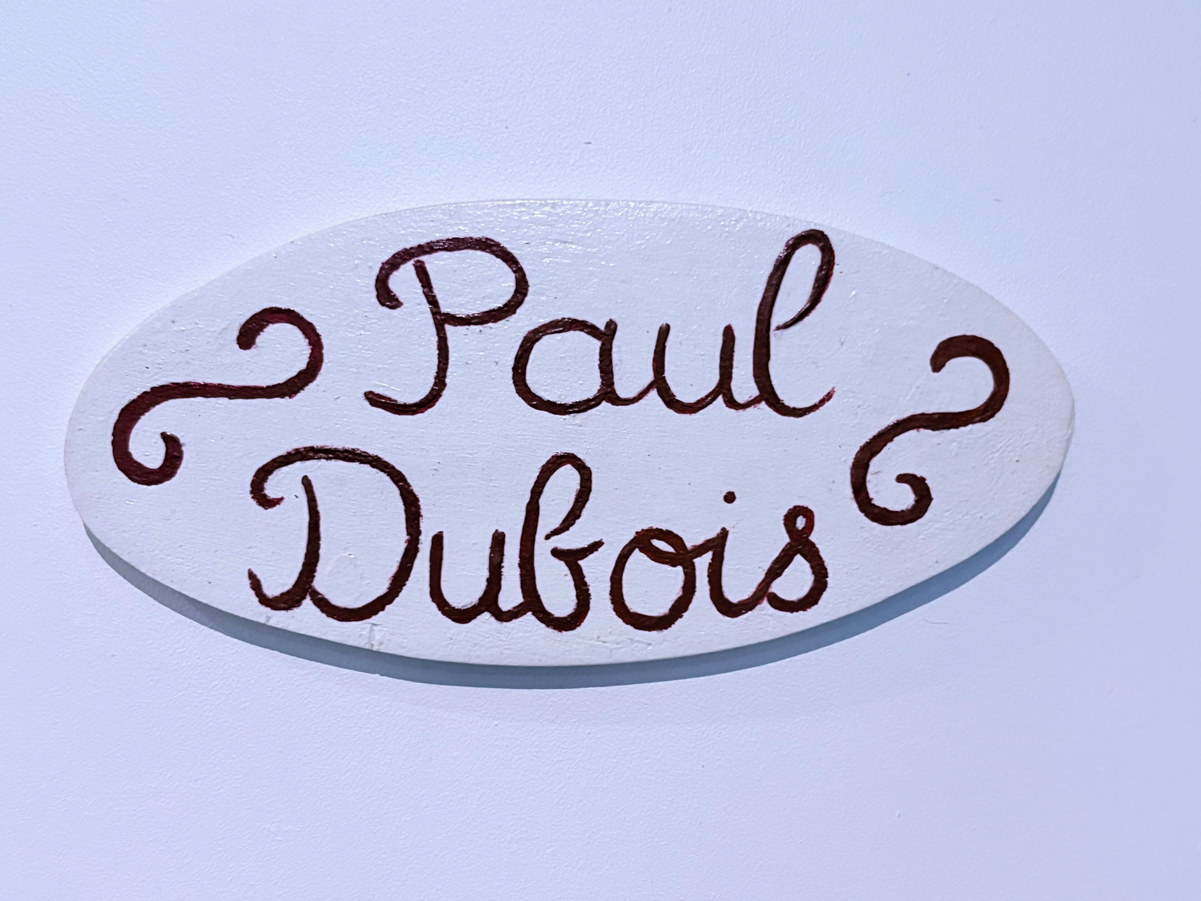 Een witte ovale plaquette met de naam 'Paul Dubois' in bruine letters.