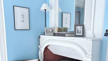 A room with a fireplace, a brown leather armchair, a side table with books, and framed pictures on the wall.