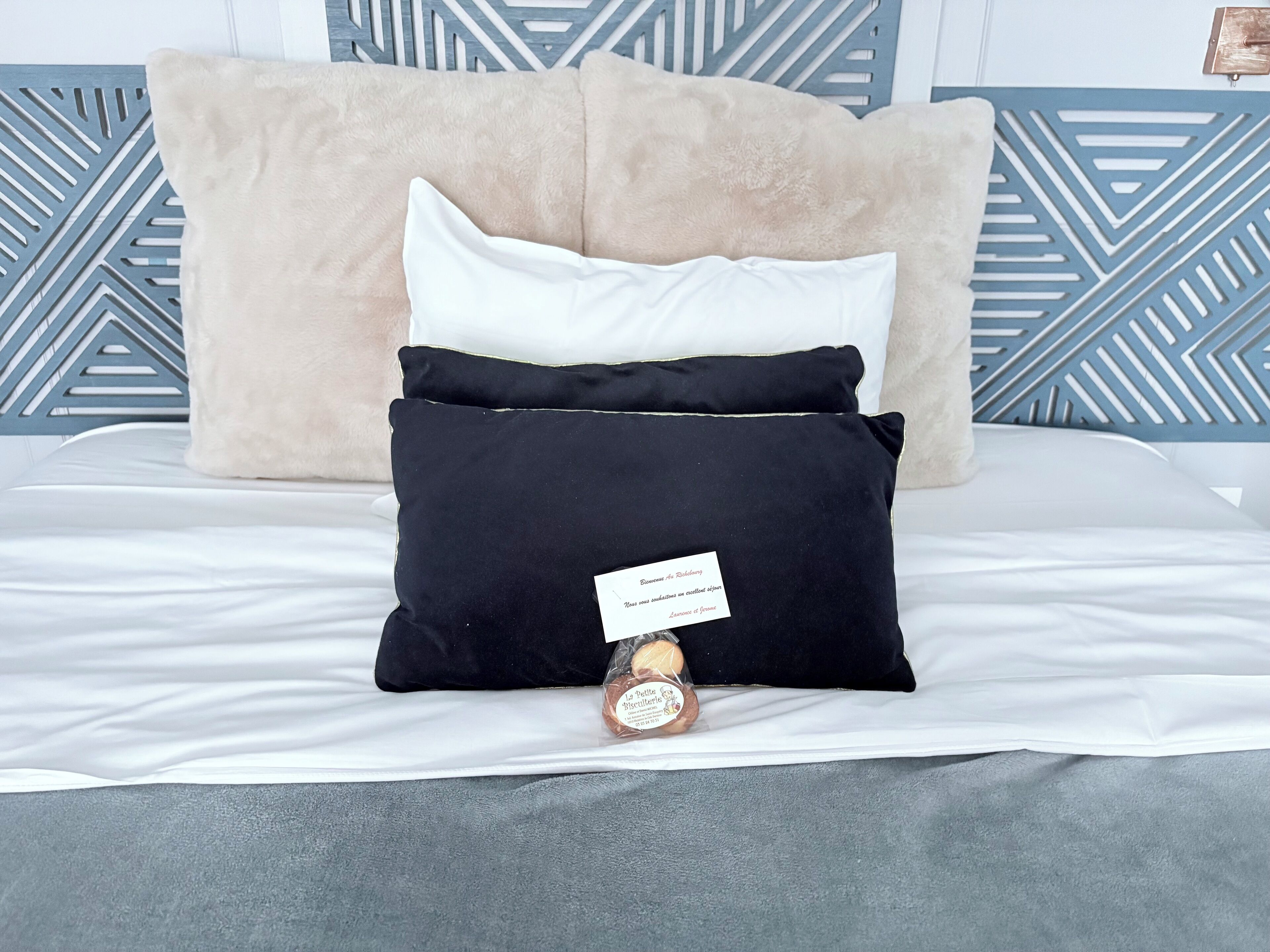 A bed with a white comforter, a beige pillow, a black pillow, and a white pillow.