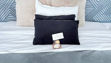 A bed with a white comforter, a beige pillow, a black pillow, and a white pillow.