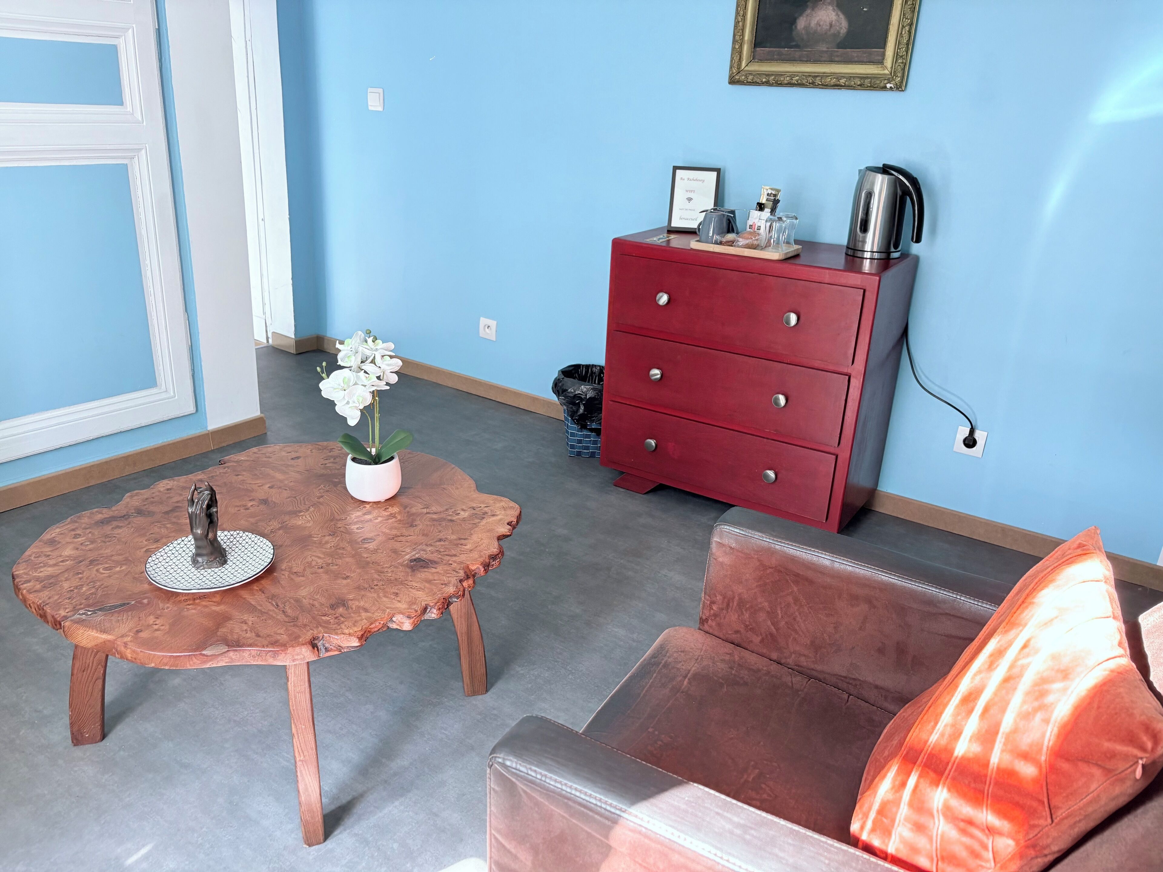 Una habitación con una mesa redonda de madera, un aparador rojo, un sofá de cuero marrón y una orquídea en maceta.