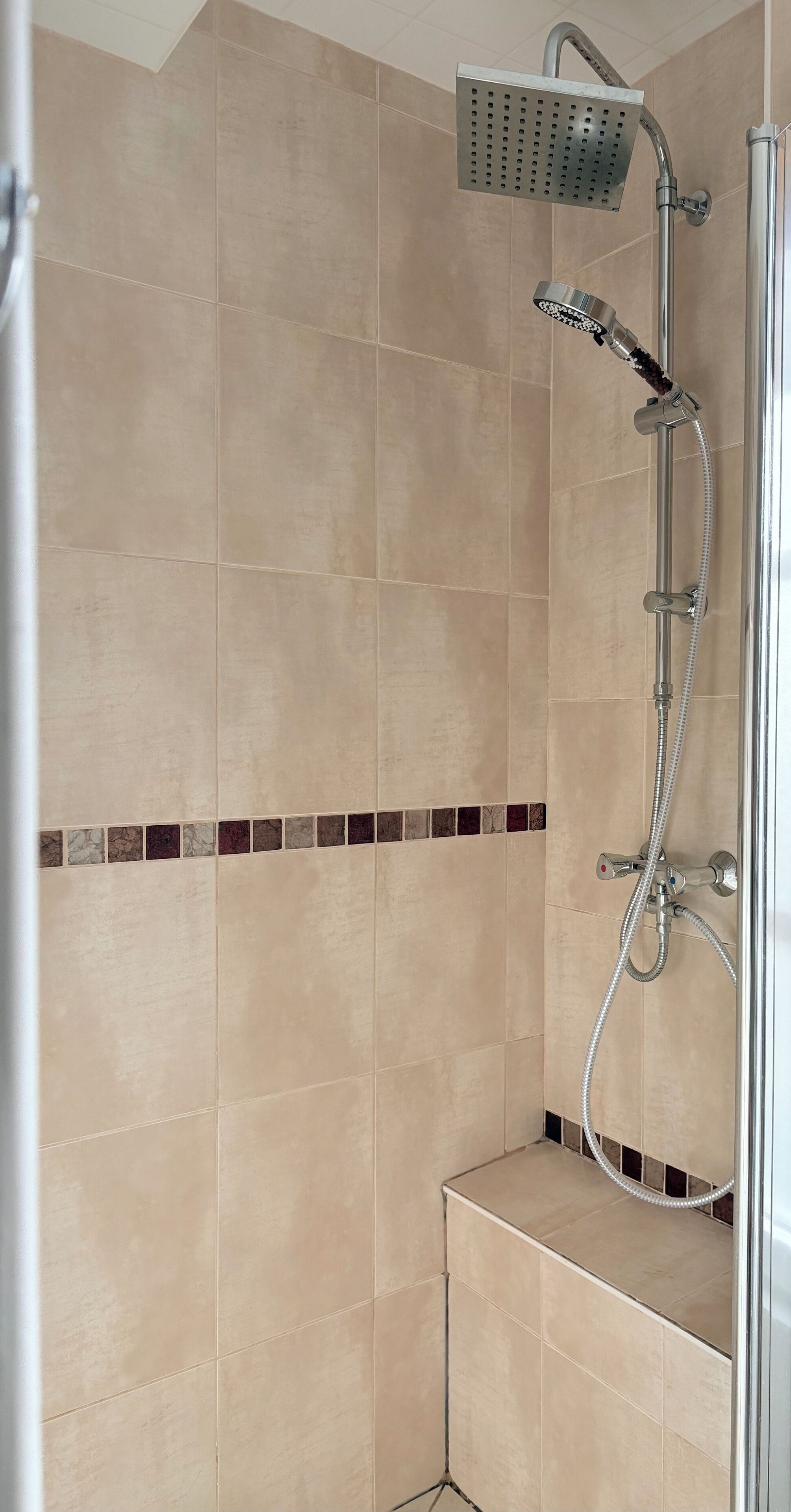 A shower area with beige tiles, a handheld showerhead, and a wall-mounted showerhead.