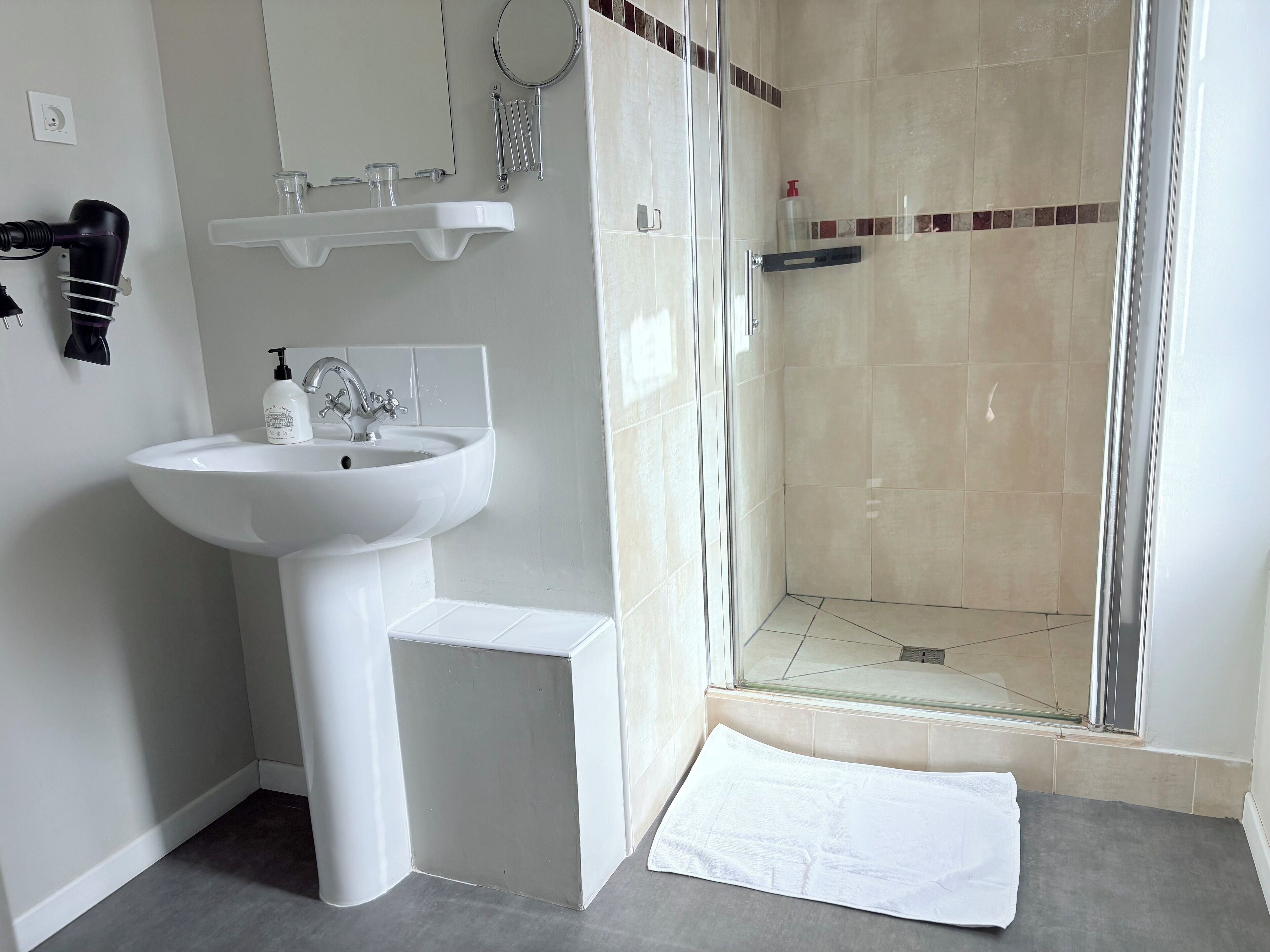 A bathroom with a white sink, a mirror, a hairdryer, and a shower area.