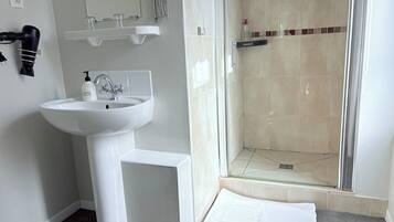 A bathroom with a white sink, a mirror, a hairdryer, and a shower area.