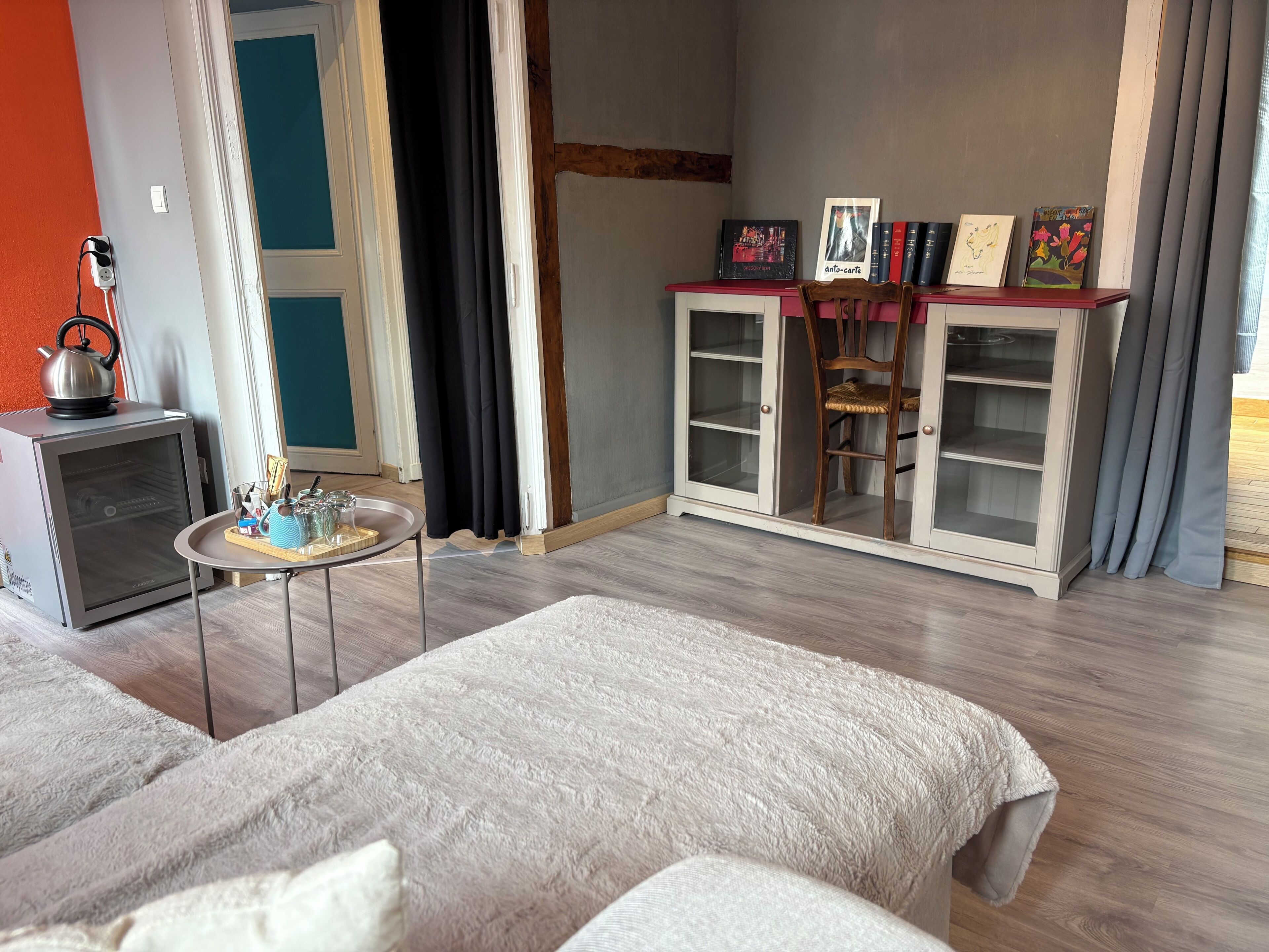Una habitación moderna con sofá, una mesita con tetera, un armario con libros y una ventana con cortinas.