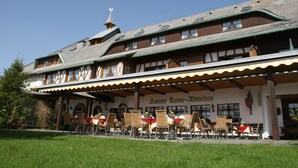 Un bâtiment traditionnel de Bavière doté d’une terrasse, une enseigne indiquant « Haisers Tanne-Wirtshaus », et un ciel dégagé.