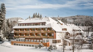 Un hôtel à plusieurs étages, dont le toit est recouvert de neige et qui possède de nombreux balcons, entouré d’un paysage enneigé et d’arbres.