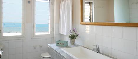 A bathroom with a large white sink, a mirror, and a view of the sea through the windows.