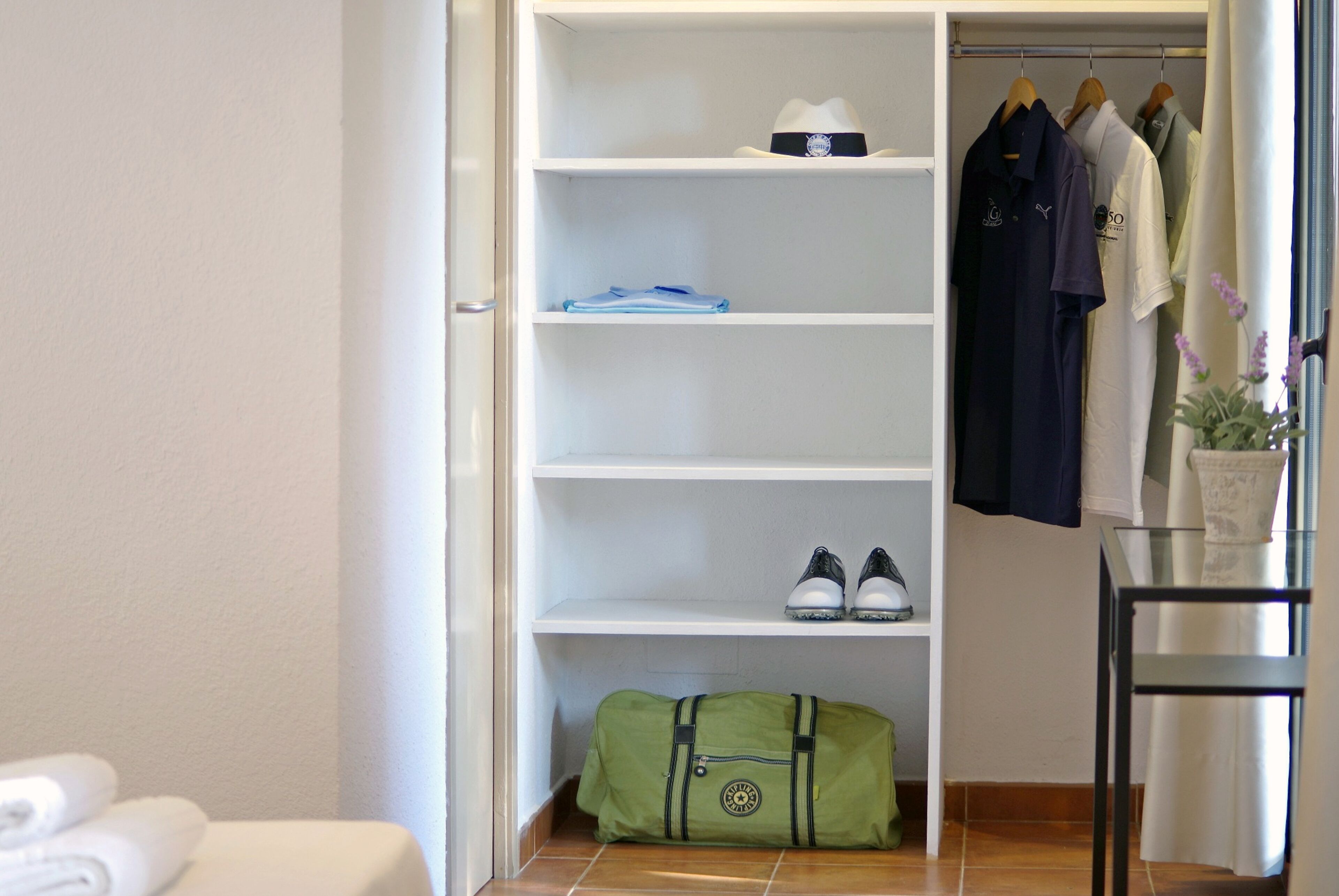 Un dressing avec des étagères, une tringle à vêtements et un sac de sport vert.
