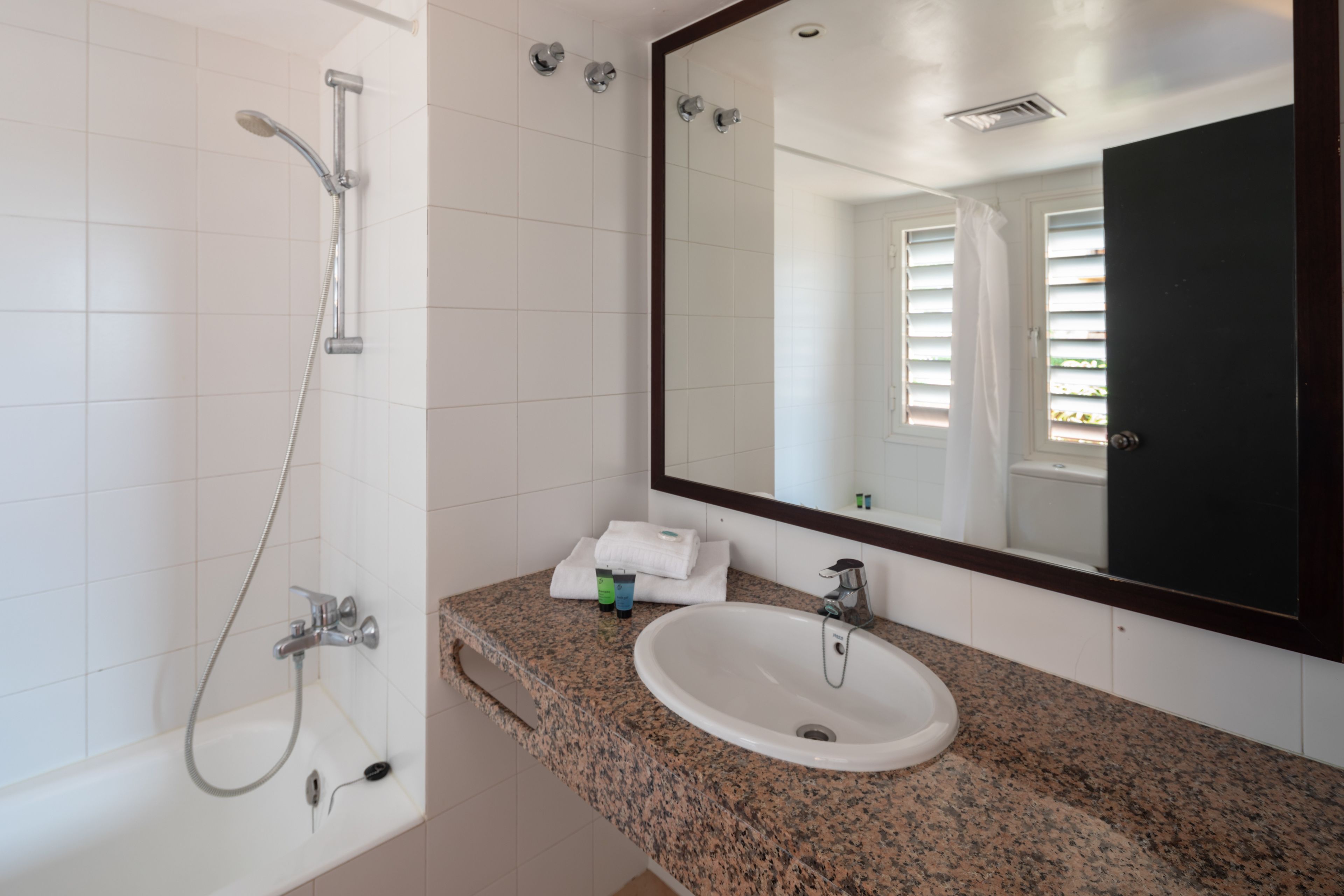 Un bagno con una vasca da bagno bianca, un piano di lavoro in granito, un lavandino e uno specchio grande.