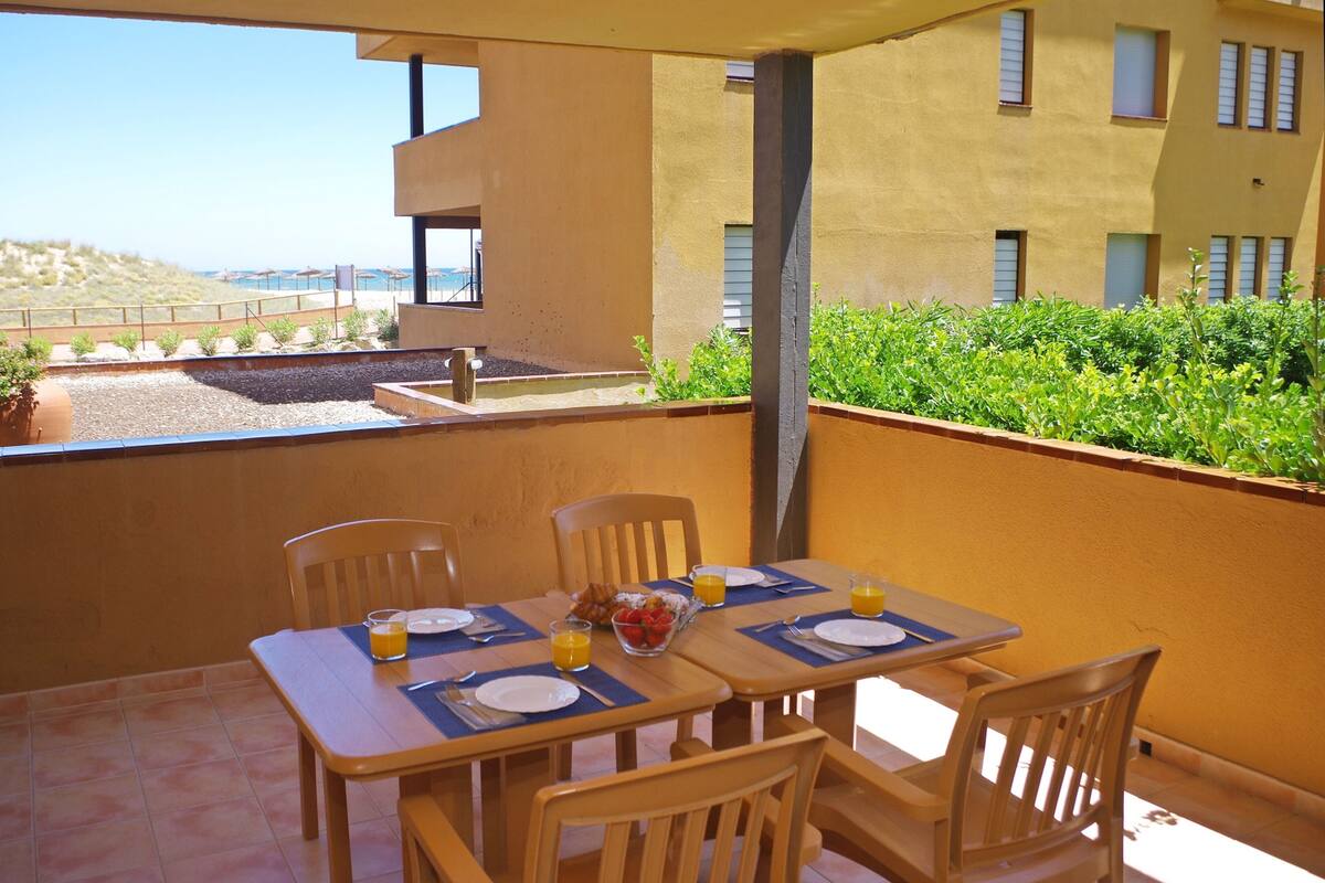 A dining area with a table set for two, a bowl of fruit, and a view of the sea.