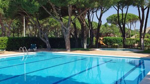 A swimming pool with clear blue water, surrounded by trees and a fenced area. - Apartamentos Beach & Golf Resort (Pals)