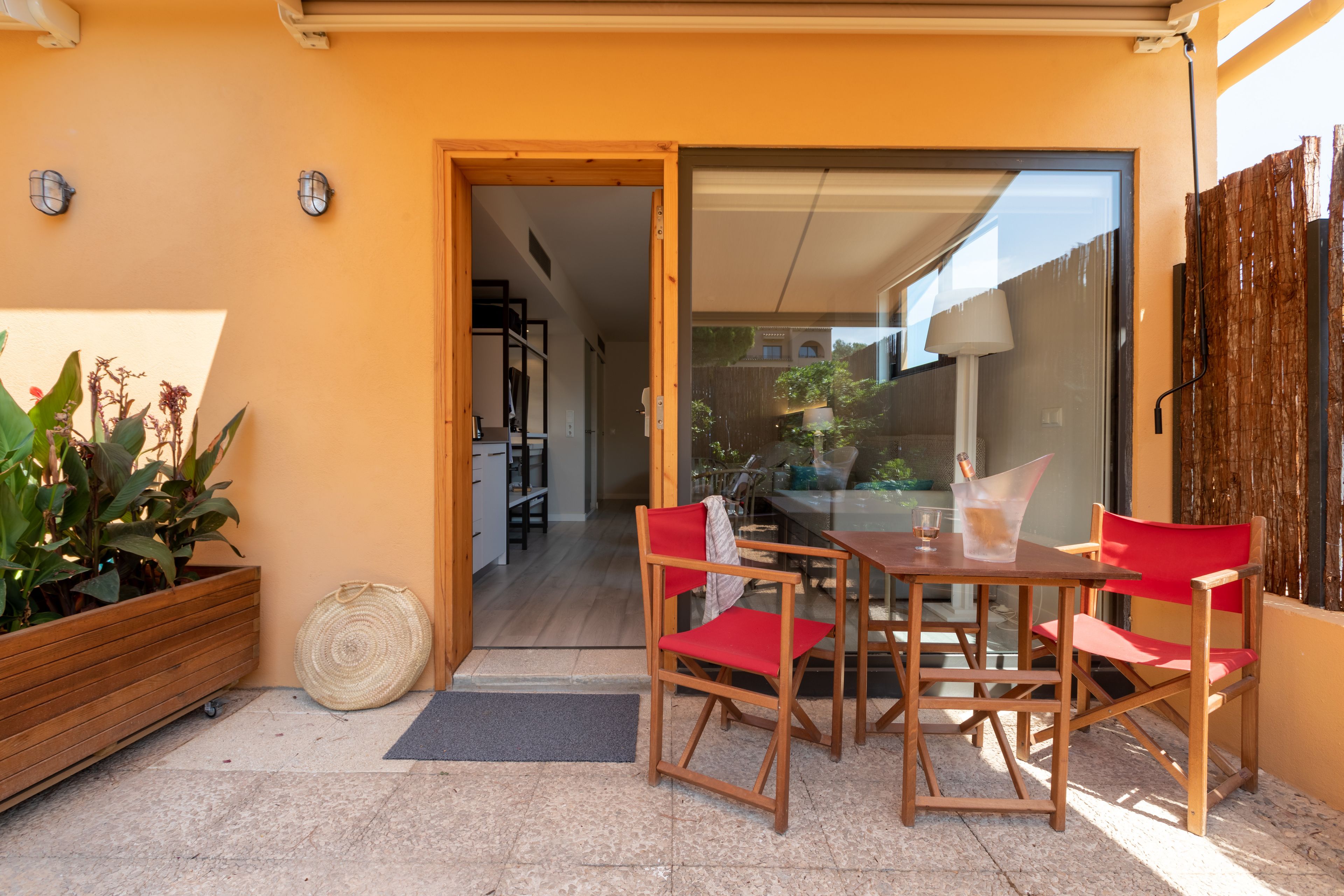 Een terras met een tafel, stoelen, een houten plantenbak en een deur naar een keuken.