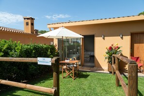 A bungalow with a patio, a wooden table, and a white umbrella. - Apartamentos Beach & Golf Resort (Pals)