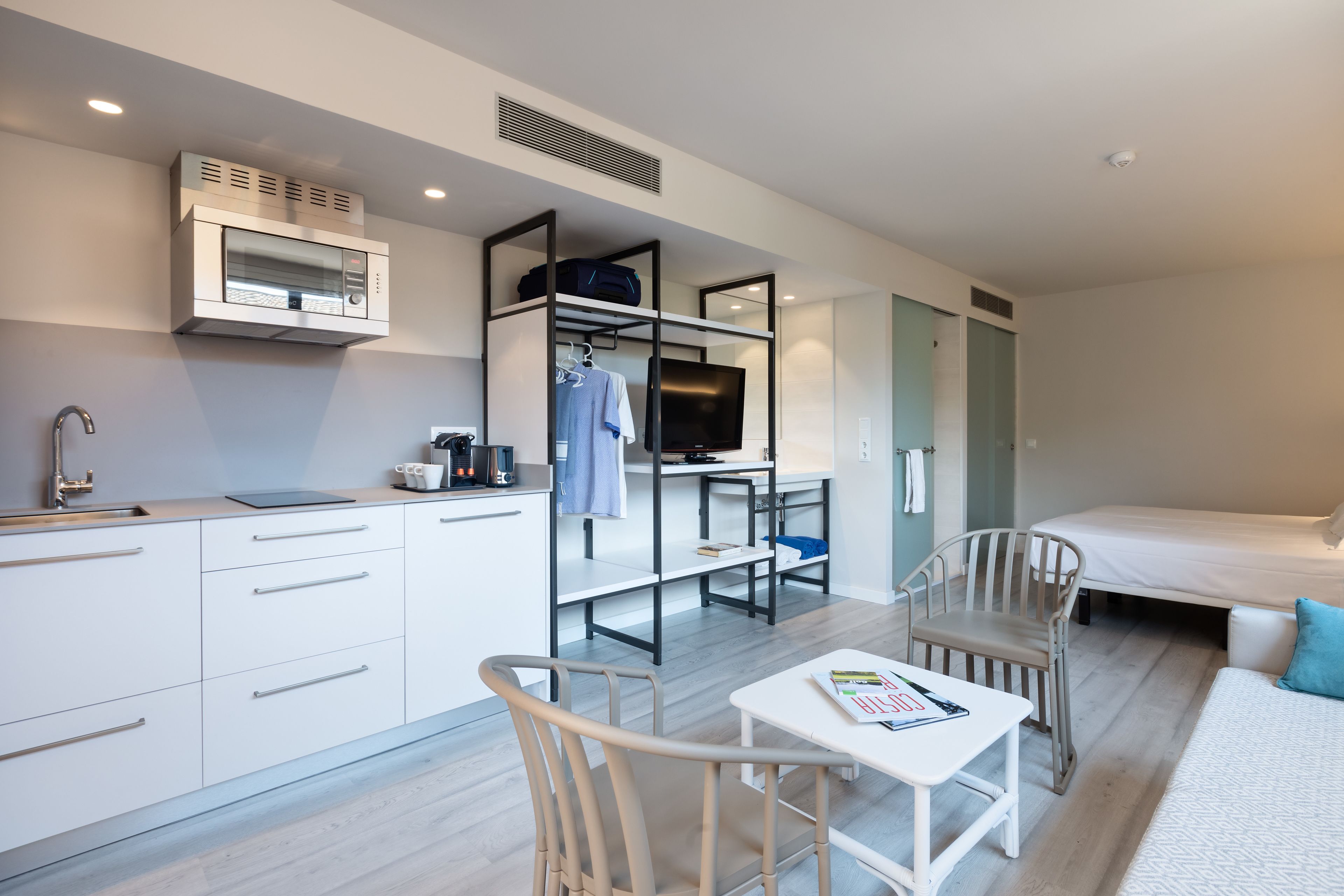 Une chambre d’hôtel de taille réduite, équipée d’une kitchenette, d’un lit, d’un bureau et d’une chaise.
