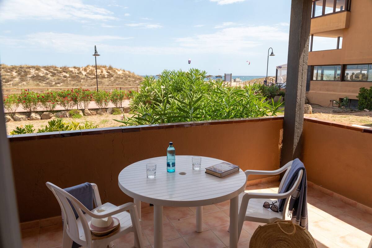 A round table with chairs on a balcony overlooking a beach.