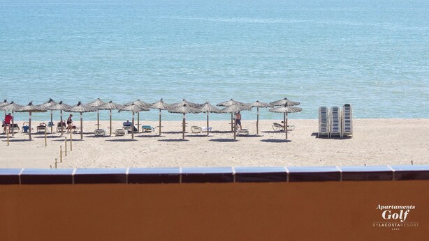 A beach with rows of sun umbrellas and lounge chairs, a clear view of the sea, and a sign for 'Apartments Golf by Lacostaresort'. - Apartamentos Beach & Golf Resort (Pals)