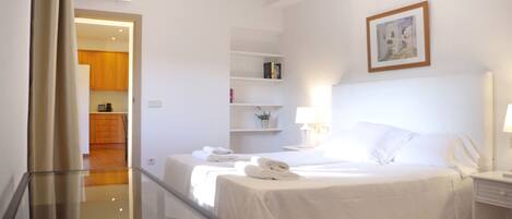 A hotel room with a bed, bedside tables, a lamp, a shelf with books, and a painting on the wall.