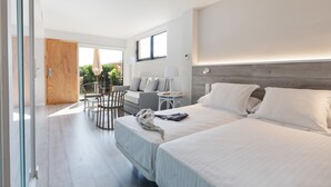 A modern hotel room with two beds, a sitting area with a table and chairs, a small side table, and a large window. - Apartamentos Beach & Golf Resort (Pals)